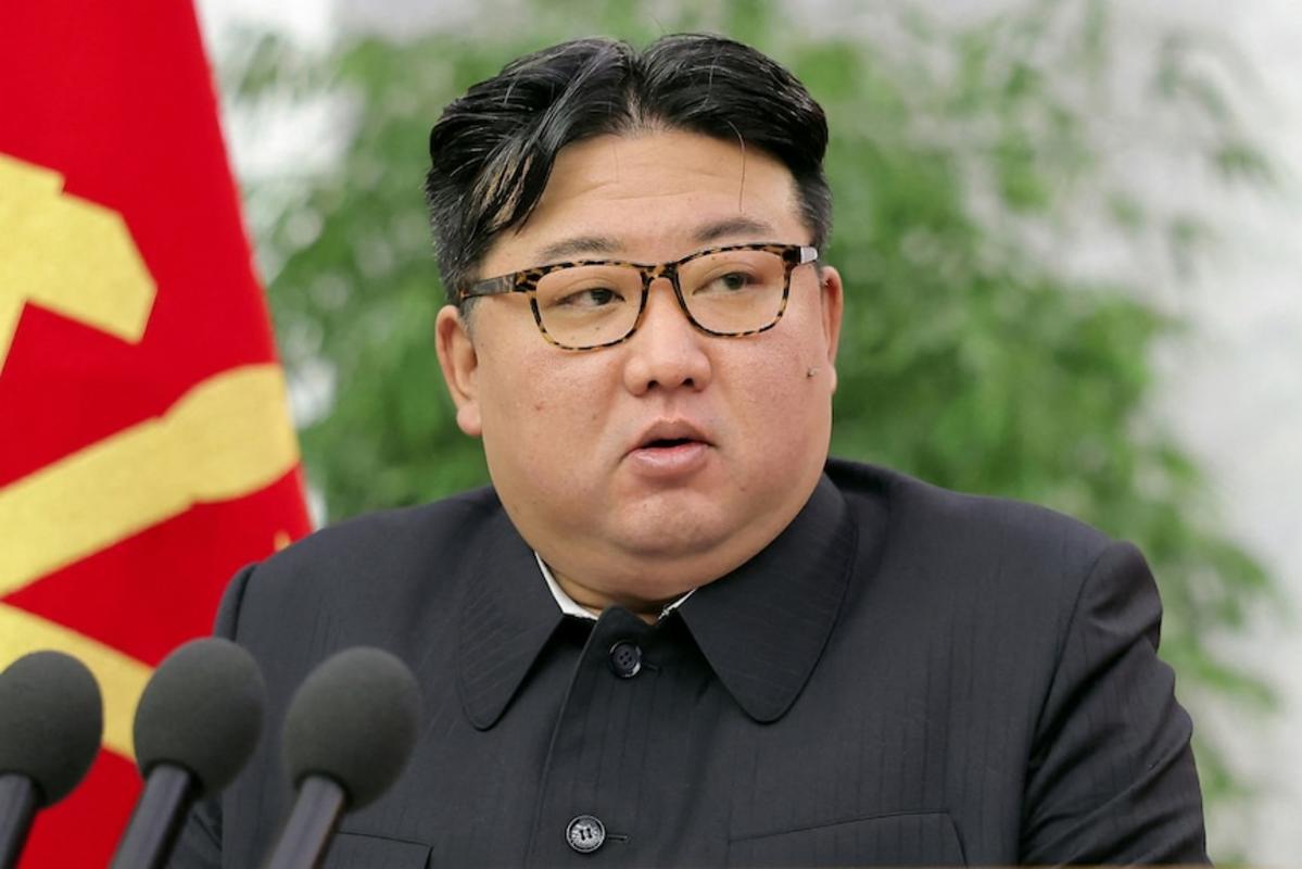 Kim Jong Un phát biểu trước micro với lá cờ đỏ và vàng ở phía sau