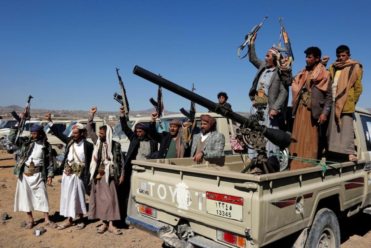 Các chiến binh và người bộ lạc Houthi đứng trên và xung quanh một chiếc xe bán tải cầm súng.