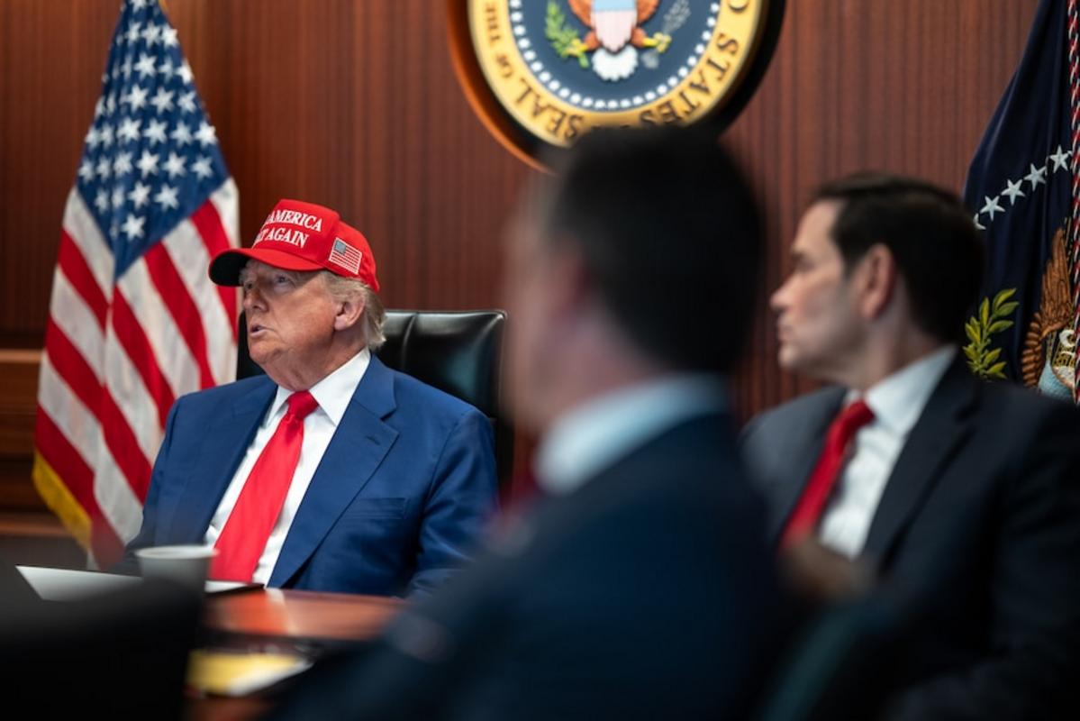 Trump ngồi ở bàn hội nghị bên cạnh hai người đàn ông mặc vest đen